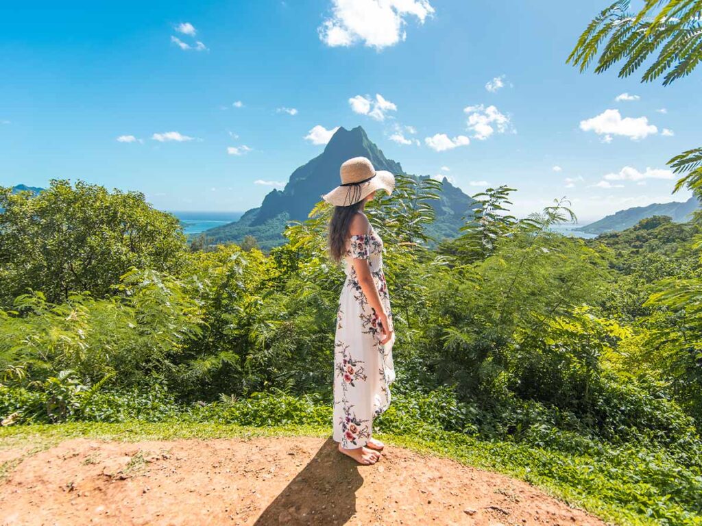 Touriste admirant le belvédère de Moorea en Polynésie française, offrant une vue panoramique sur les montagnes et le lagon tropical sous un ciel bleu clair.