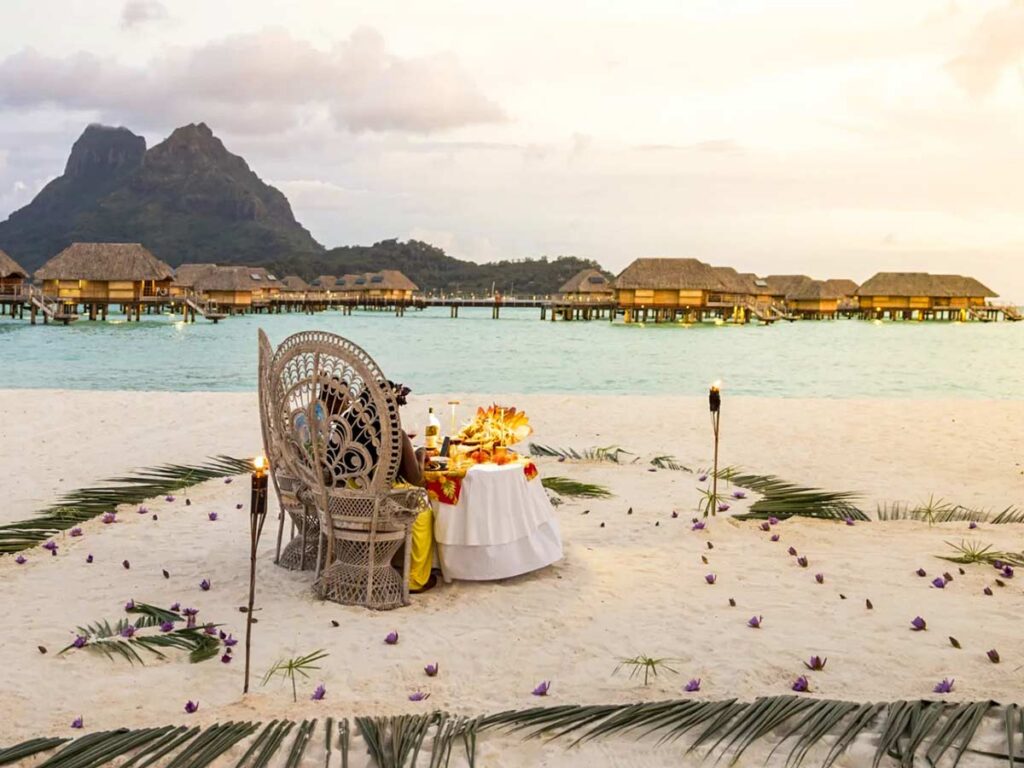 Dîner romantique sur un motu privé à Bora Bora, avec une table élégamment dressée au bord du lagon, entourée de sable blanc et offrant une vue sur le coucher de soleil.