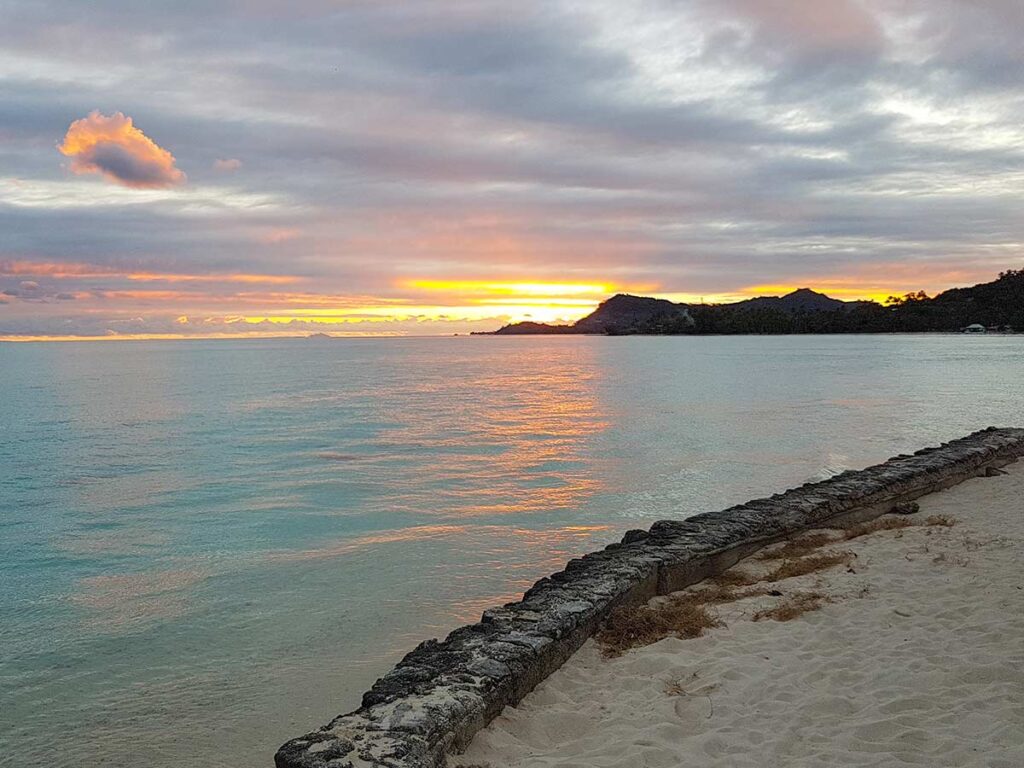 Coucher de soleil sur la plage de Matira à Bora Bora, illuminant le ciel de nuances orange, rose et violet, se reflétant sur les eaux cristallines du lagon bordé de sable blanc.