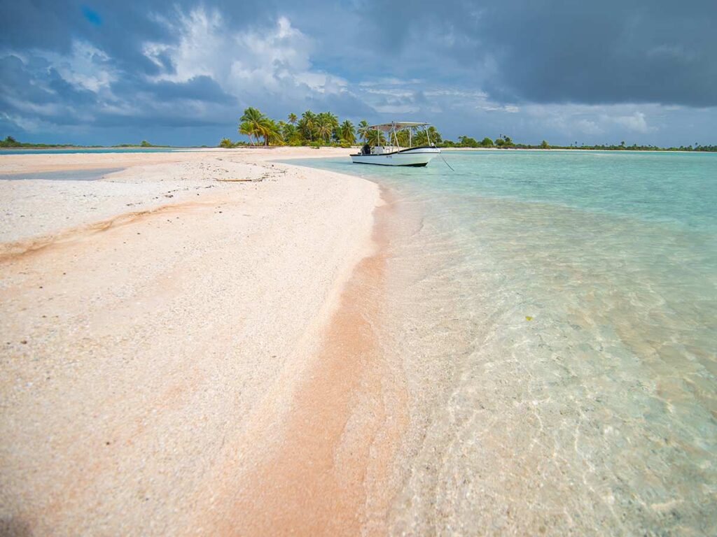 Plage de sable rose à Tikehau en Polynésie française, bordée par un lagon turquoise aux eaux cristallines, offrant un cadre naturel exceptionnel.