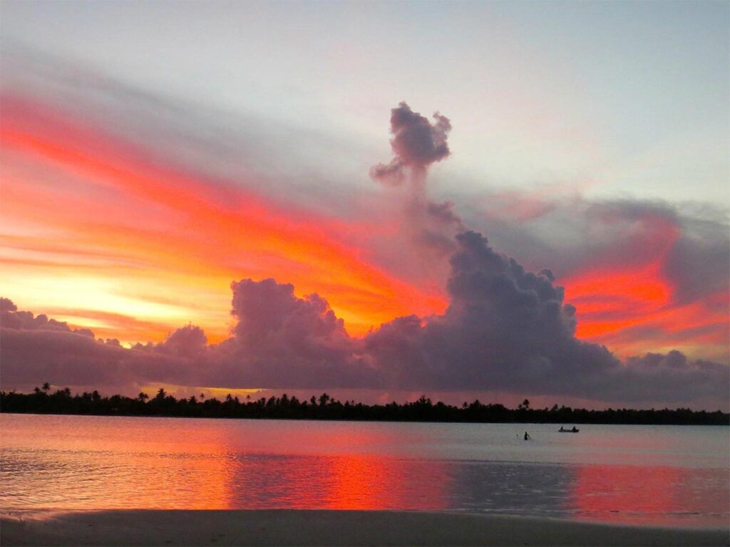 Soleil couchant à Maupiti illuminant le lagon et les palmiers dans une atmosphère sereine.