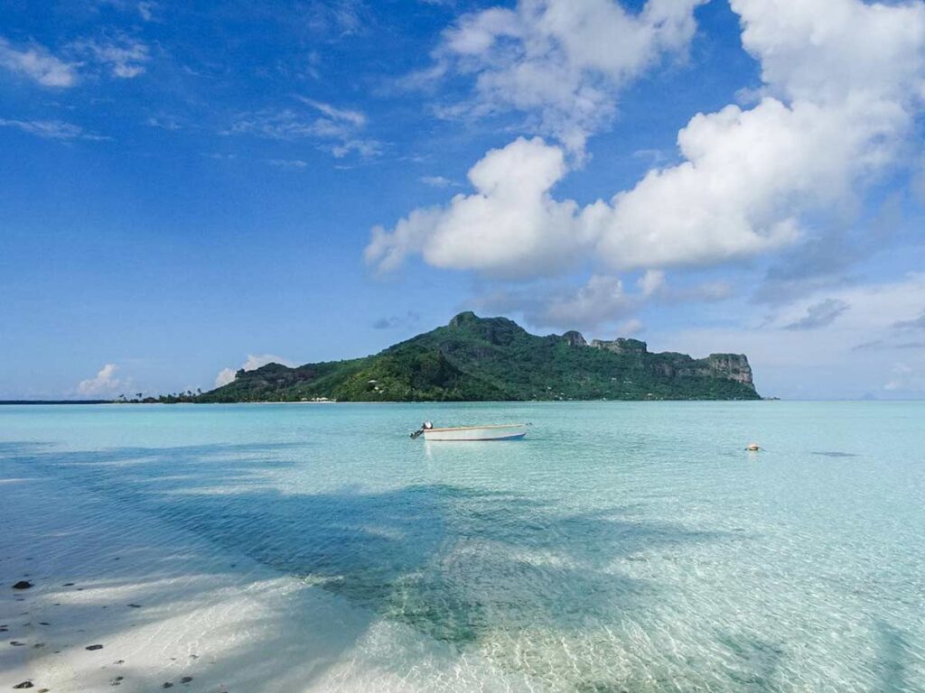 Panorama sur le motu Auira depuis le sable blanc de la plage de Tereia, avec le lagon turquoise en premier plan.