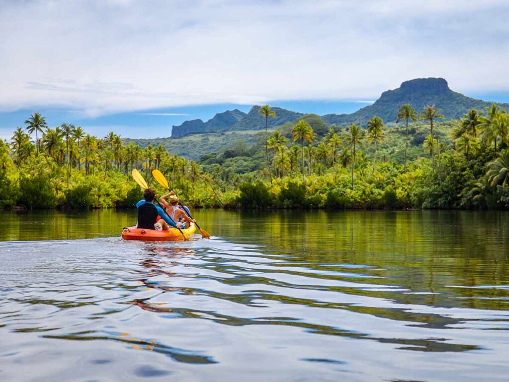 Rivière Faaroa à Raiatea, en Polynésie française, bordée de végétation tropicale luxuriante avec deux personnes qui font du kayak.