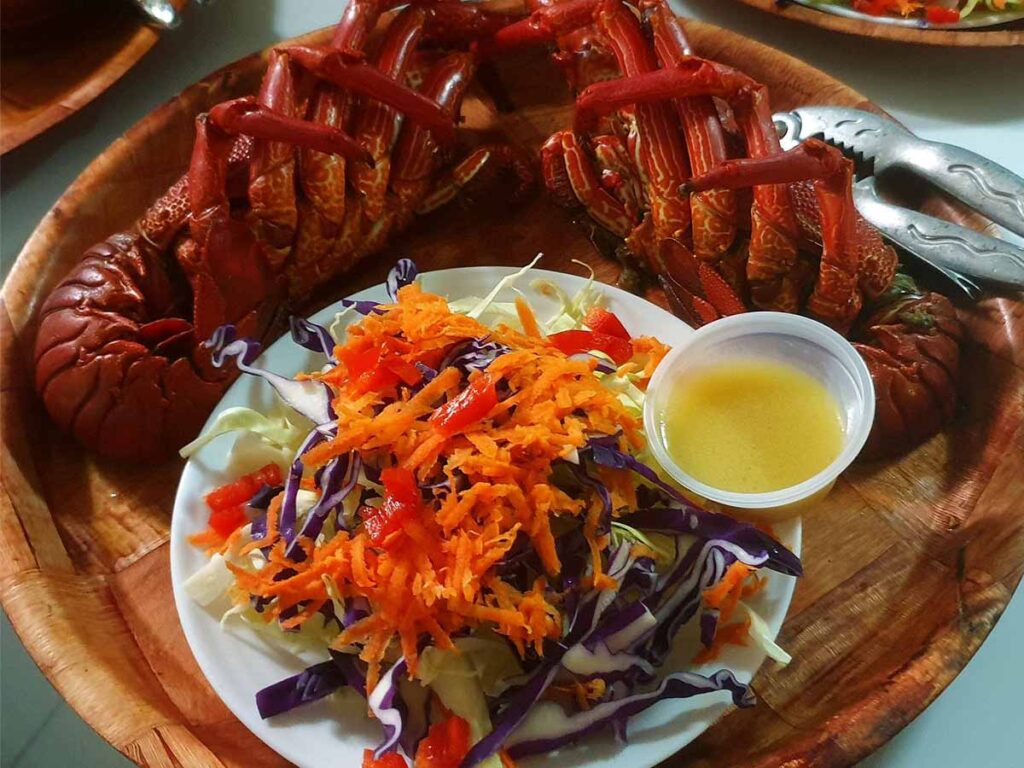 Assiette de langouste servie au Snack Rangiroa Plage à Rangiroa, avec accompagnements locaux dans un cadre en bord de lagon.