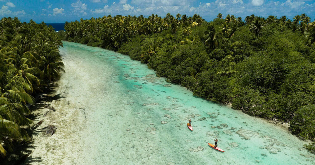 Groupe de personnes faisant du paddle dans le lagon cristallin de Tetiaroa, pour une expérience immersive en pleine nature polynésienne.